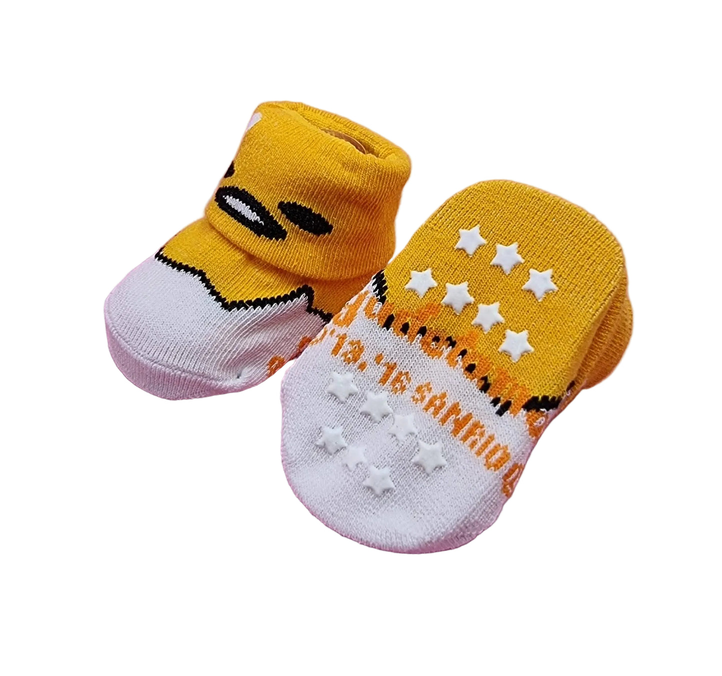 A pair of baby socks designed to look like Gudetama, featuring a yellow knit upper with embroidered black eyes and mouth, and a white knit lower with raised white stars and orange text, displayed on a pink background.