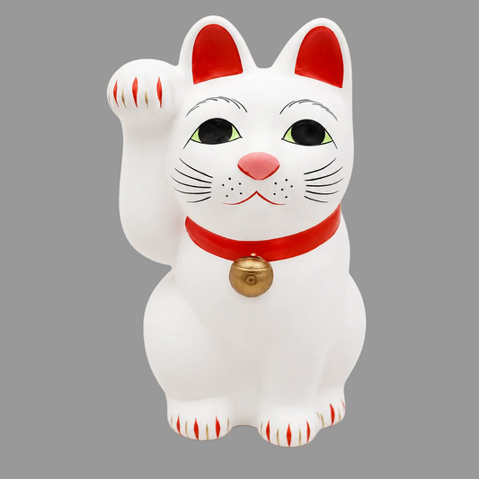 A white Japanese maneki-neko lucky cat figurine with a raised paw, featuring red accents on its ears, paws, and collar, a pink nose, and a small gold bell.